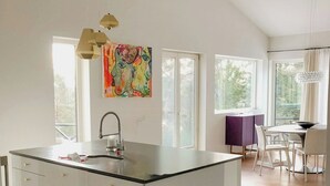 A modern kitchen with a central island, large windows, and a dining area with chairs. - Modern Design Villa on Älgö Island (Saltsjöbaden)