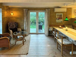 Ein gemütliches Zimmer mit Esstisch, Korbstühlen, einem Glastisch, einem Teppich und Blick durch eine Glastür auf eine Terrasse.
