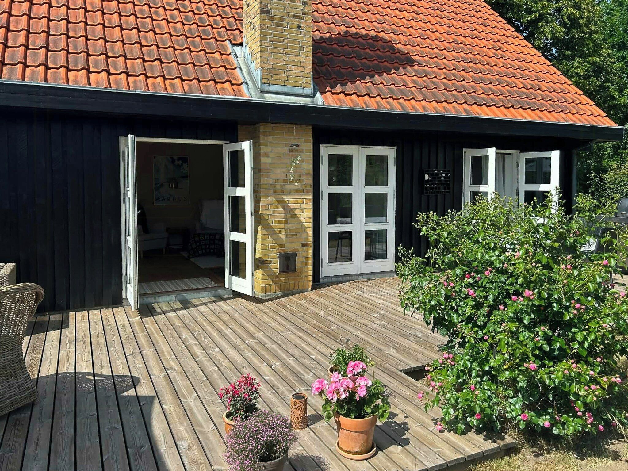 A wooden deck with potted plants, a brick wall, and a red-tiled roof.