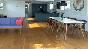 Et moderne opholdsrum med sofa, spisebord, stole, et køkken og billeder på væggene.