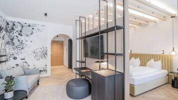 Una habitación de hotel moderna con cama, sofá, escritorio, planta en maceta y una obra de arte original en la pared.