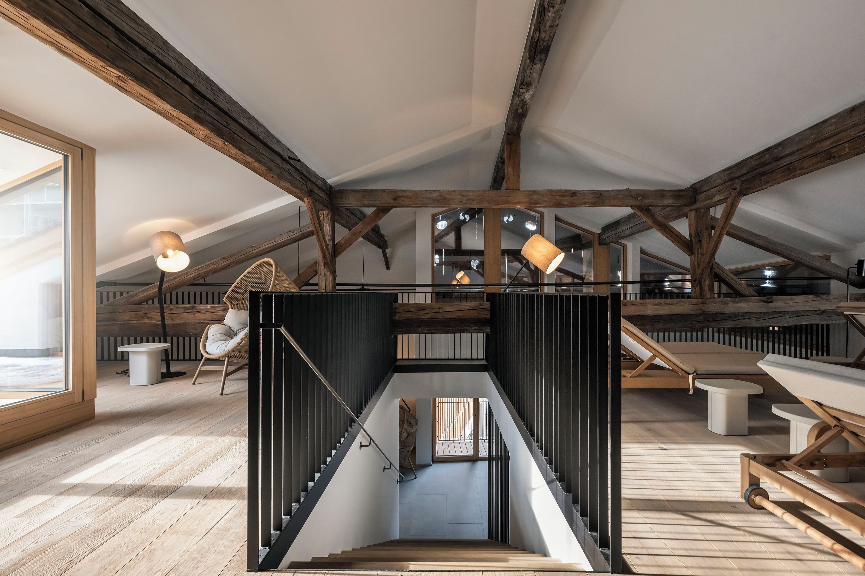 A spacious loft with exposed wooden beams, a central staircase, and a view of the sky.