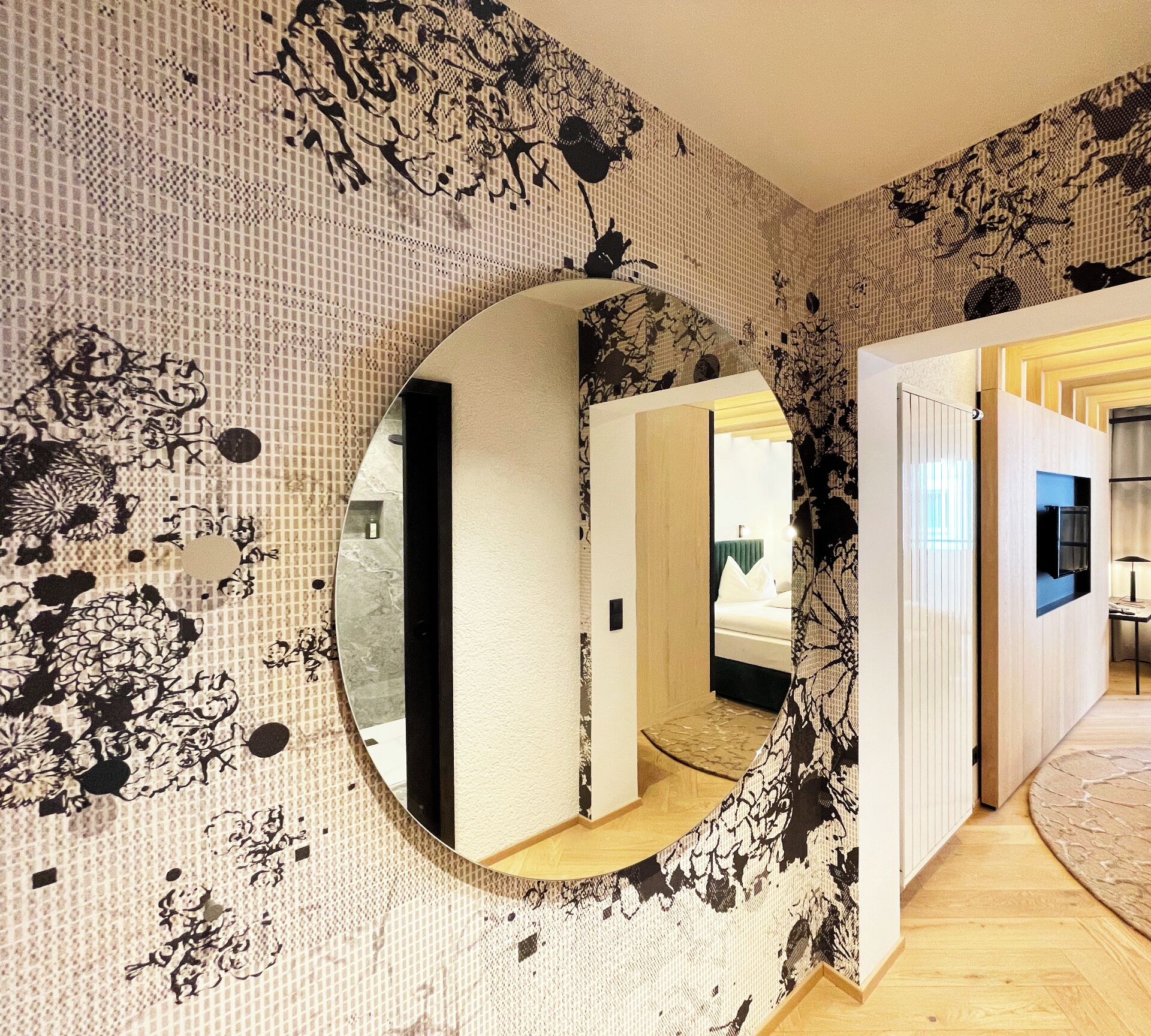A room with a large mirror, patterned wallpaper, and a wooden floor.