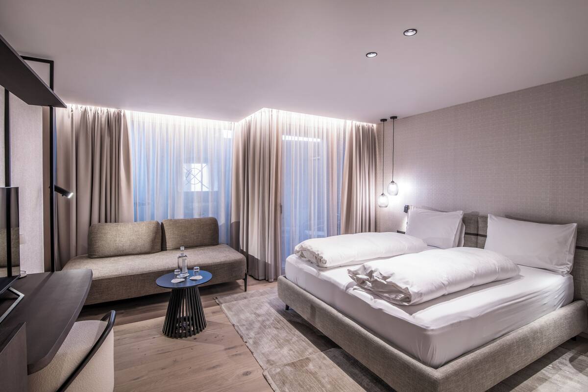 Una habitación de hotel moderna con un sofá, una cama, una mesita redonda y un televisor.