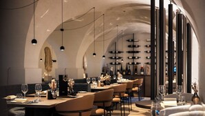 A restaurant with long tables, chairs, hanging pendant lights, and a modern interior design.