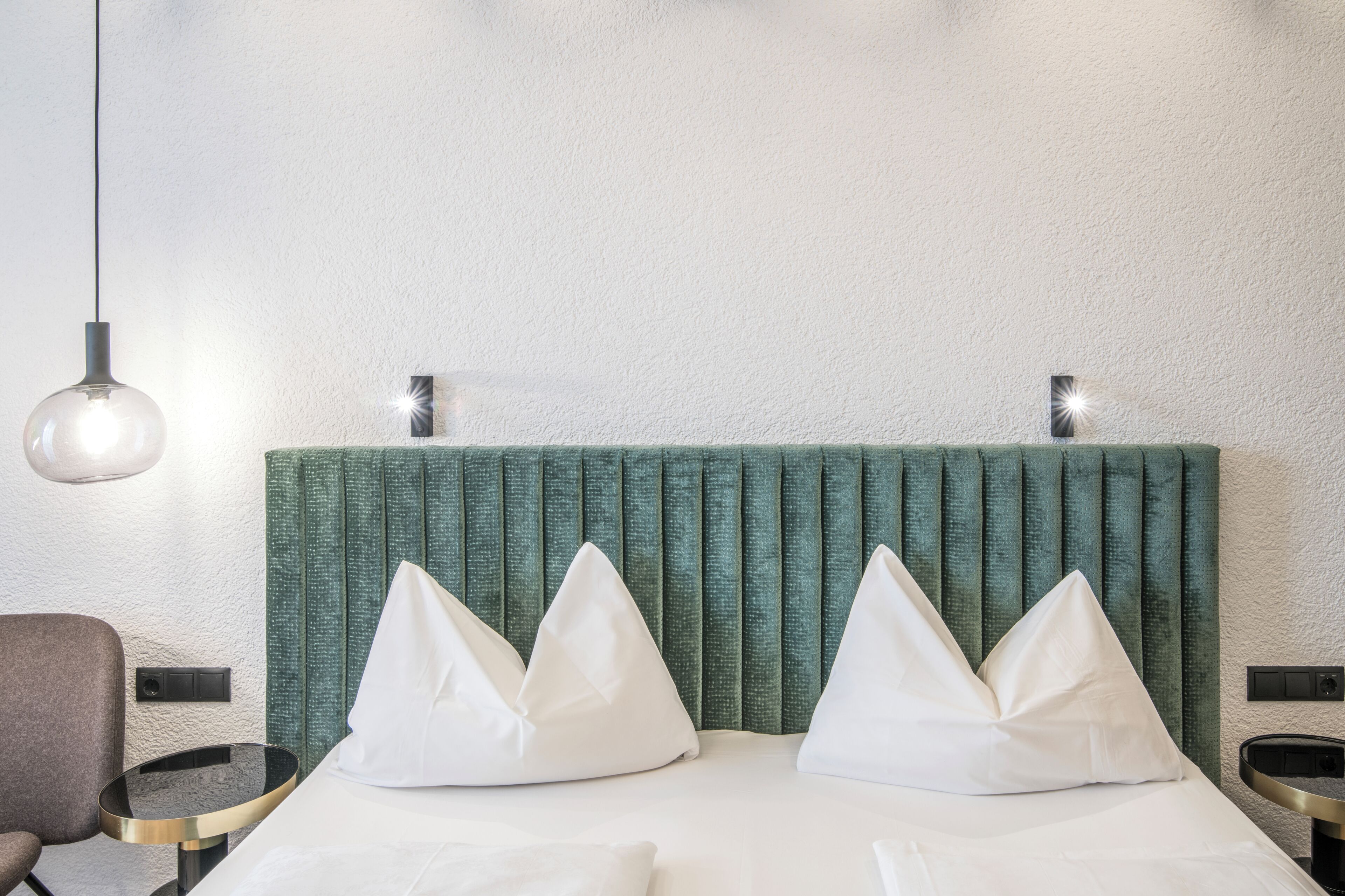 A hotel room with a bed, two bedside tables, a chair, and a hanging light fixture.