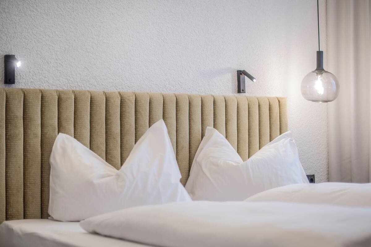 Una cama bien tendida con sábanas blancas, un cabecero texturizado y una lámpara colgante.