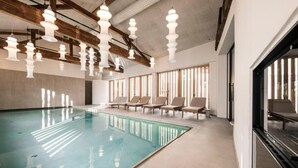 A swimming pool with lounge chairs, pendant lights, and large windows.