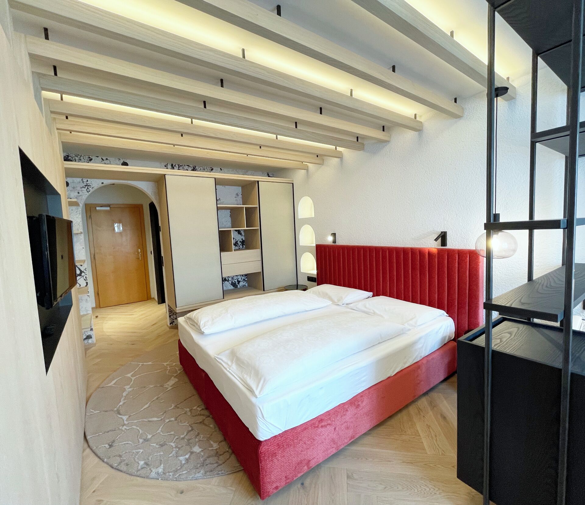 Een moderne slaapkamer met een rood bed, inbouwkasten, een televisie en een houten vloer.