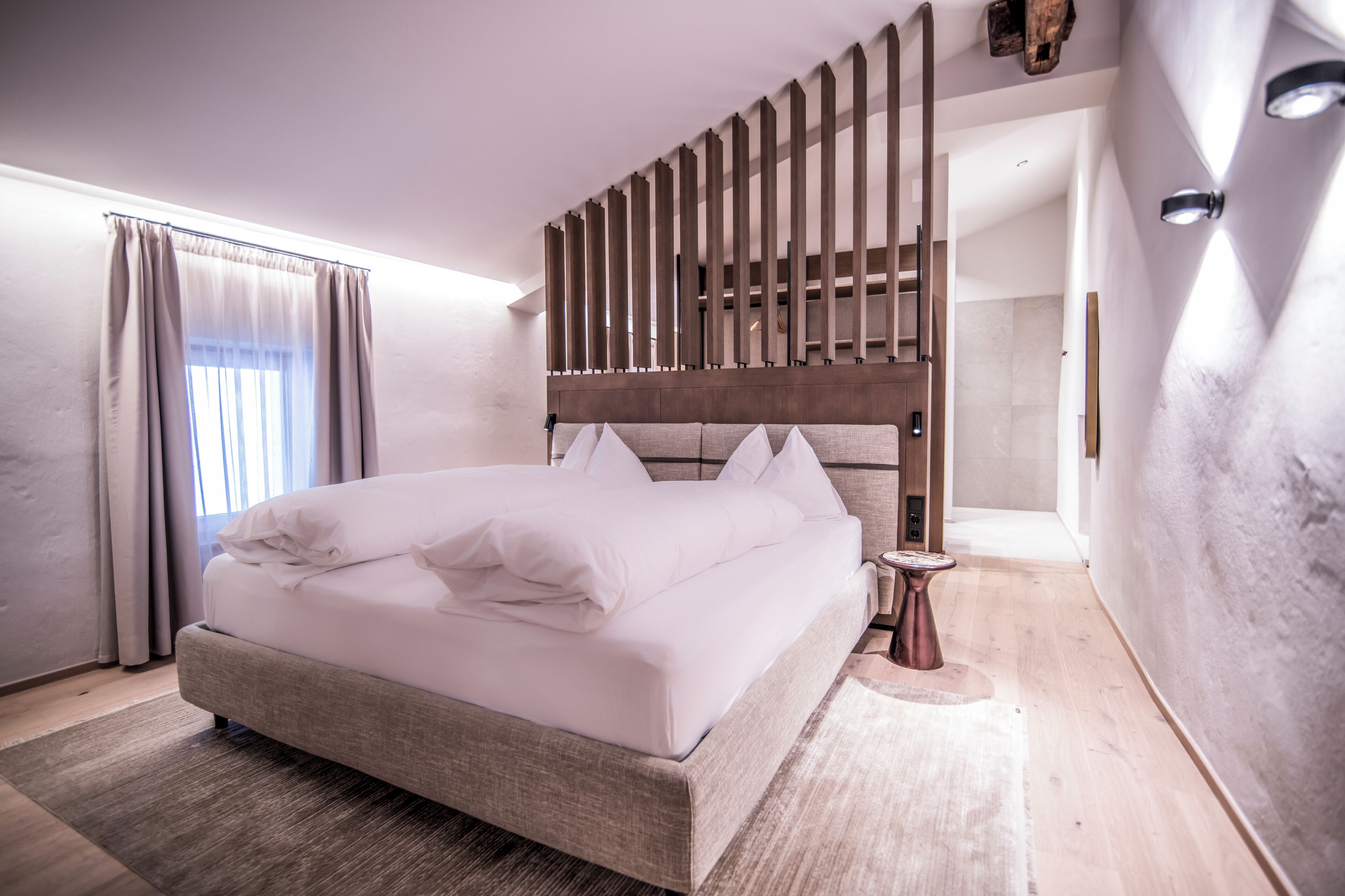 Une chambre à coucher moderne avec un grand lit, une tête de lit en bois, une table de chevet et une fenêtre avec des rideaux.