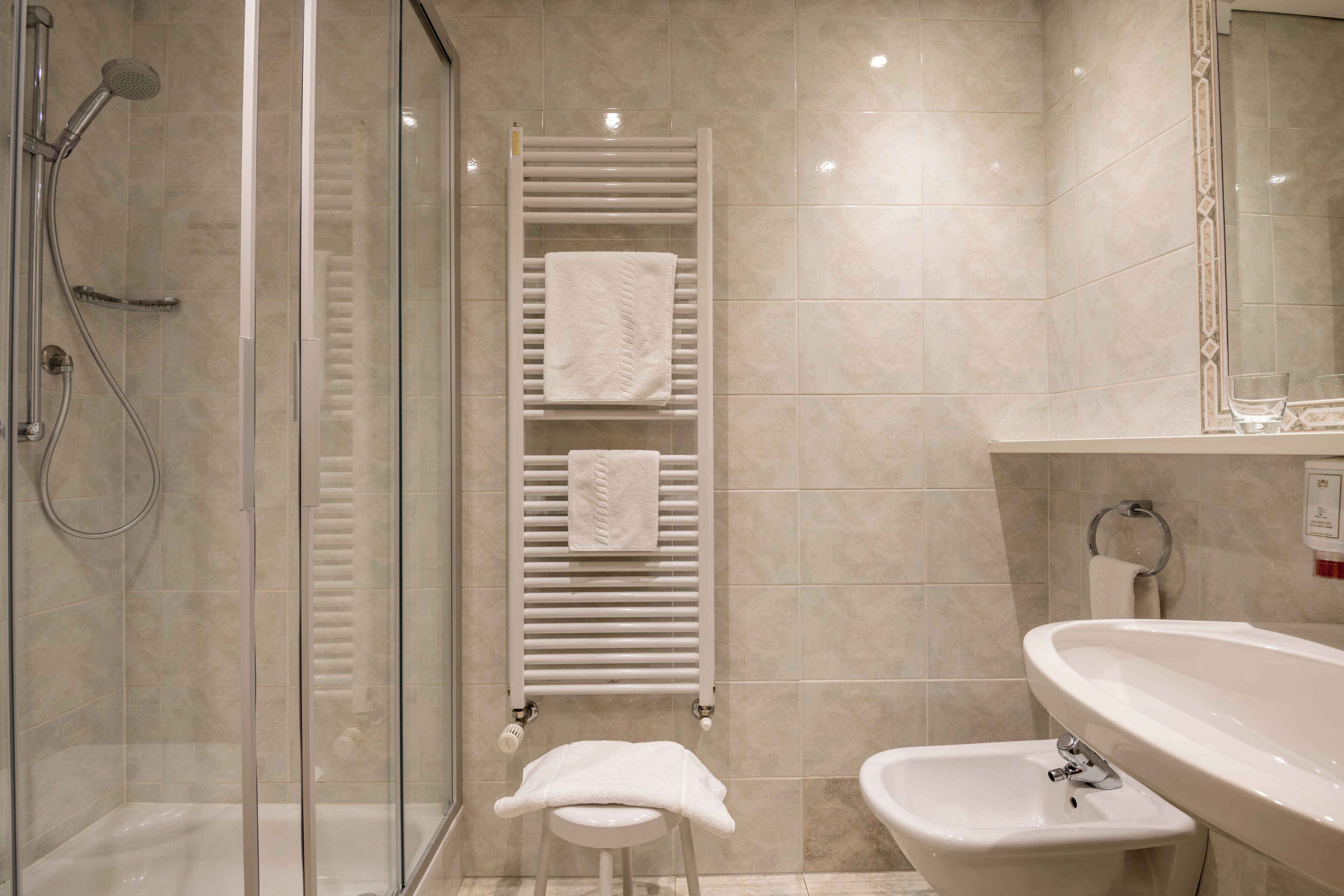 Un baño con cabina de ducha de vidrio, toallero blanco con toallas, un bidé y un lavamanos grande.
