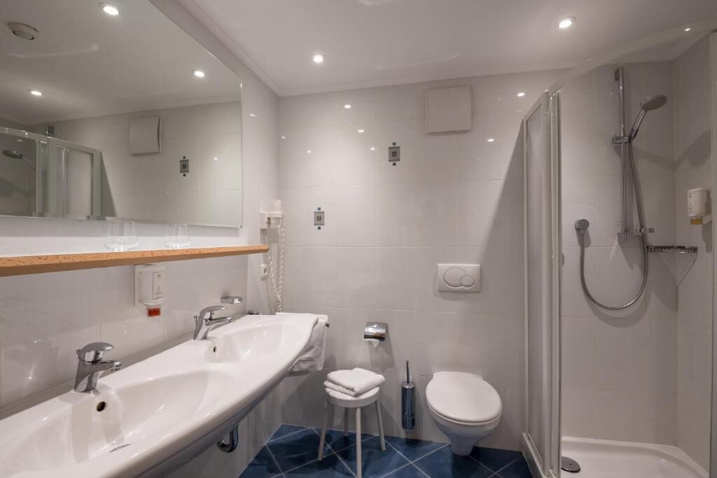 Ein modernes Badezimmer mit einem großen Spiegel, zwei Waschbecken, einer Toilette und einer Dusche.