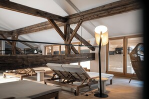 A room with wooden beams, a lounge chair, a table, and a floor lamp. - Posthotel Lamm (Vipiteno)