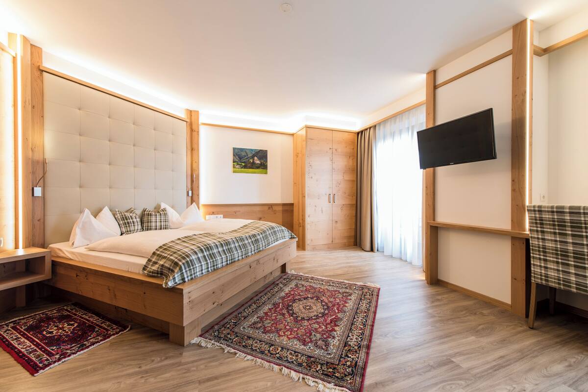 Un dormitorio con cama, cabecero de madera, mesita de noche, televisor y una alfombra de diseño rojo y azul.