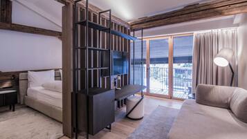 A modern hotel room with a bed, a sofa, a TV stand, and a balcony with a view.
