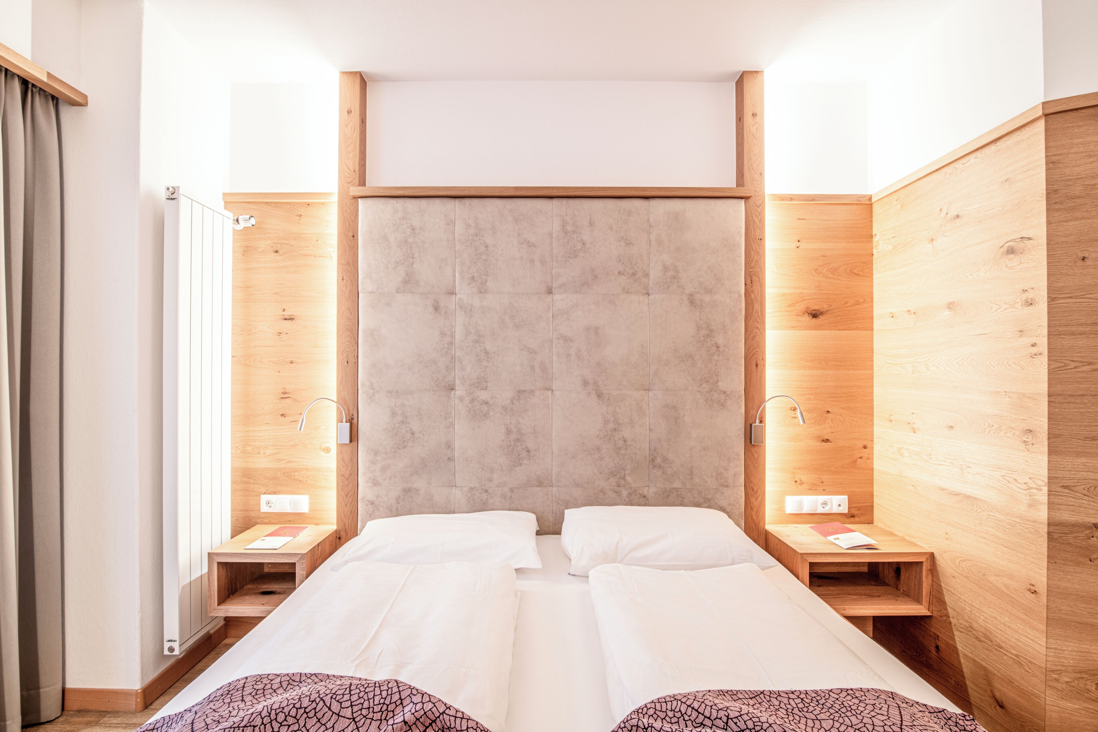 A room with two beds, wooden walls, a large window, and a radiator.