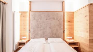 A room with two beds, wooden walls, a large window, and a radiator.