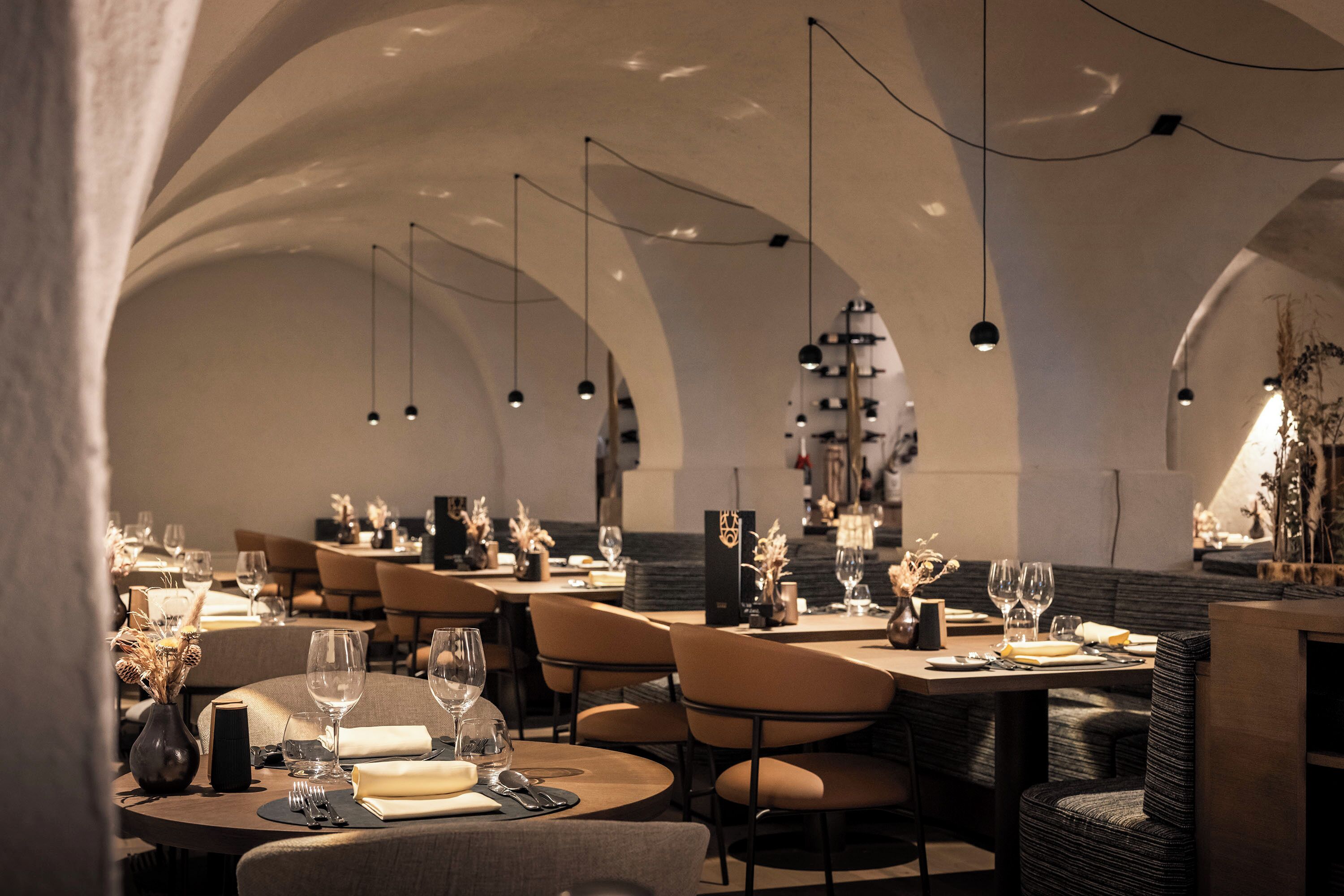 A restaurant with round tables, chairs, and hanging pendant lights.