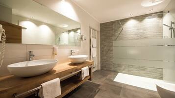 Un baño moderno con tocador de madera, dos lavamanos, un espejo grande y cabina de ducha con paredes de vidrio.