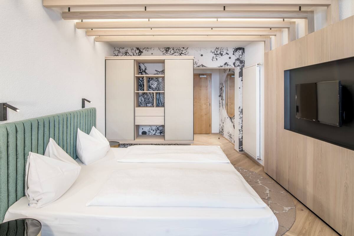 Una habitación de hotel moderna con una cama, televisión, armario y baño visible a través de una puerta abierta.
