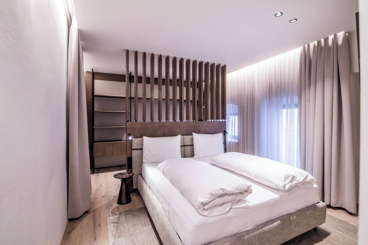 Una habitación de hotel moderna con una cama grande, un cabecero incorporado y una mesita de noche pequeña.