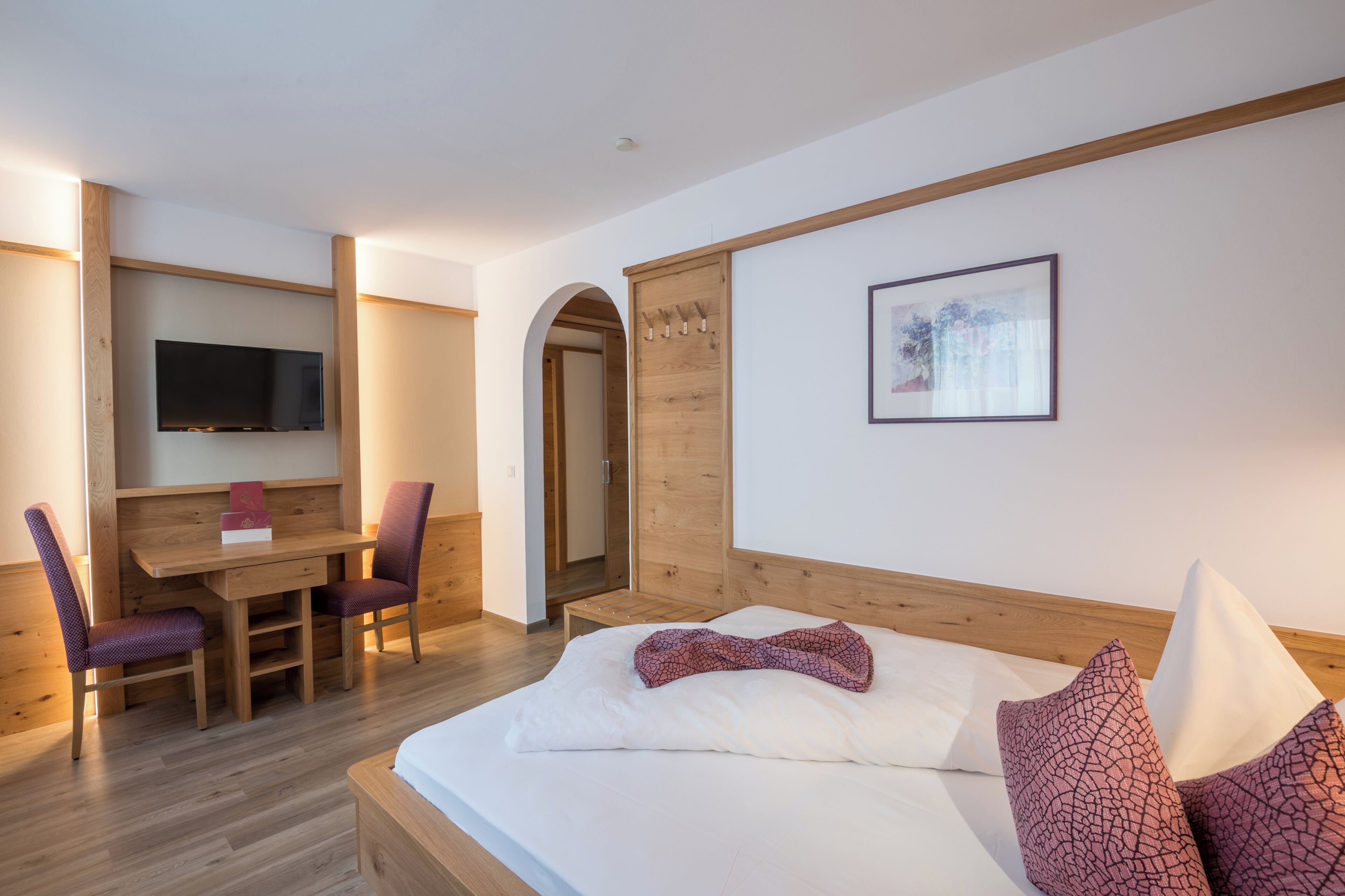Una habitación con una cama, un escritorio, dos sillas, un televisor y un armario de madera.