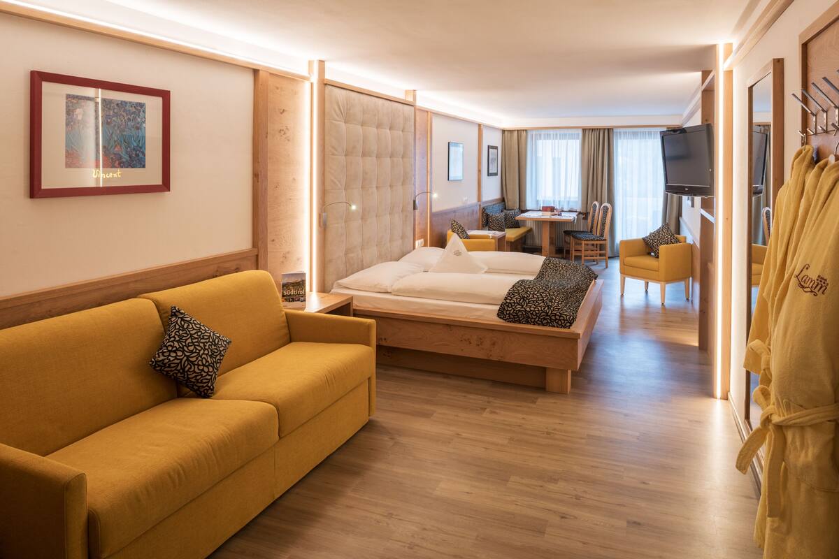 Una habitación de hotel con cama, sofá, televisor y zona de comedor.