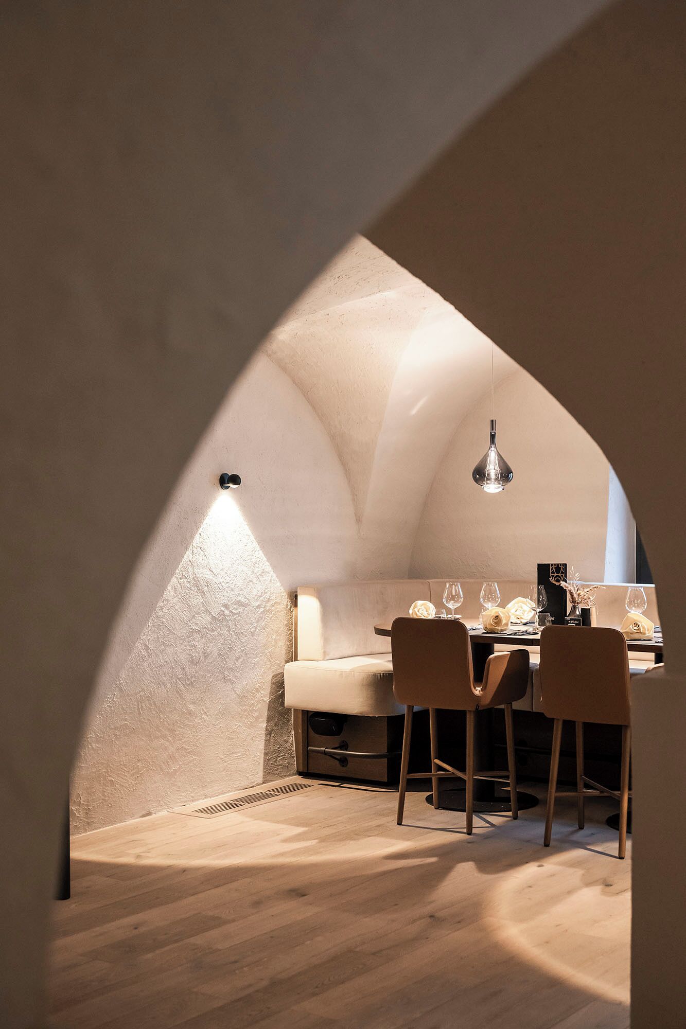 An arched dining area with a table set for two, a hanging light fixture, and a view of the outside.