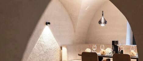 An arched dining area with a table set for two, a hanging light fixture, and a view of the outside.