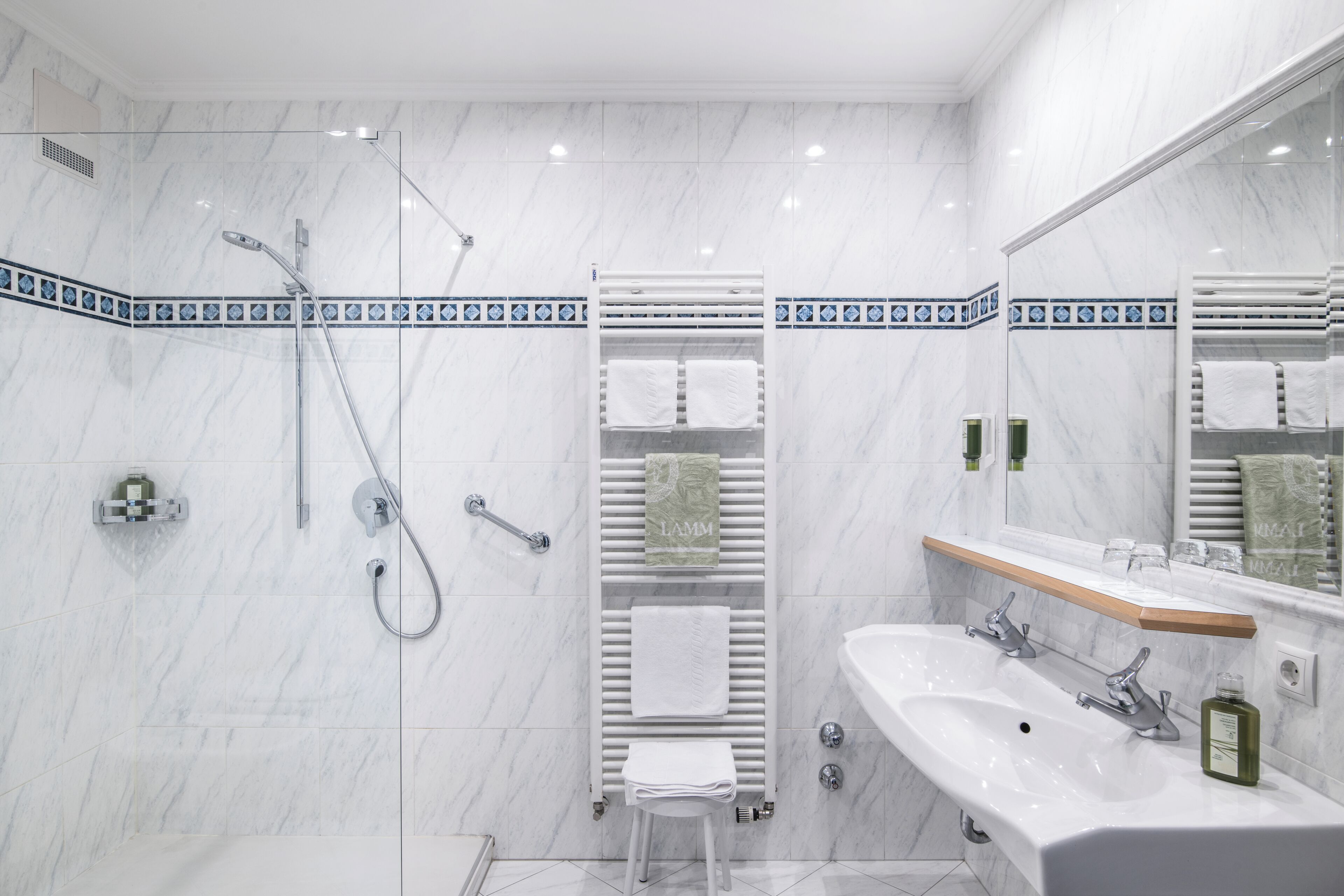 A modern bathroom with a glass-enclosed shower, a white sink, and a mirror with a wooden shelf.