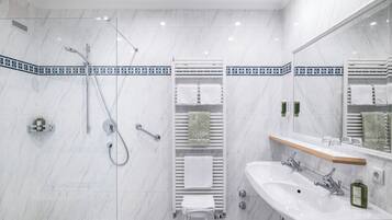A modern bathroom with a glass-enclosed shower, a white sink, and a mirror with a wooden shelf.