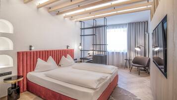 A modern hotel room with a red upholstered bed, a desk, a chair, and a television.