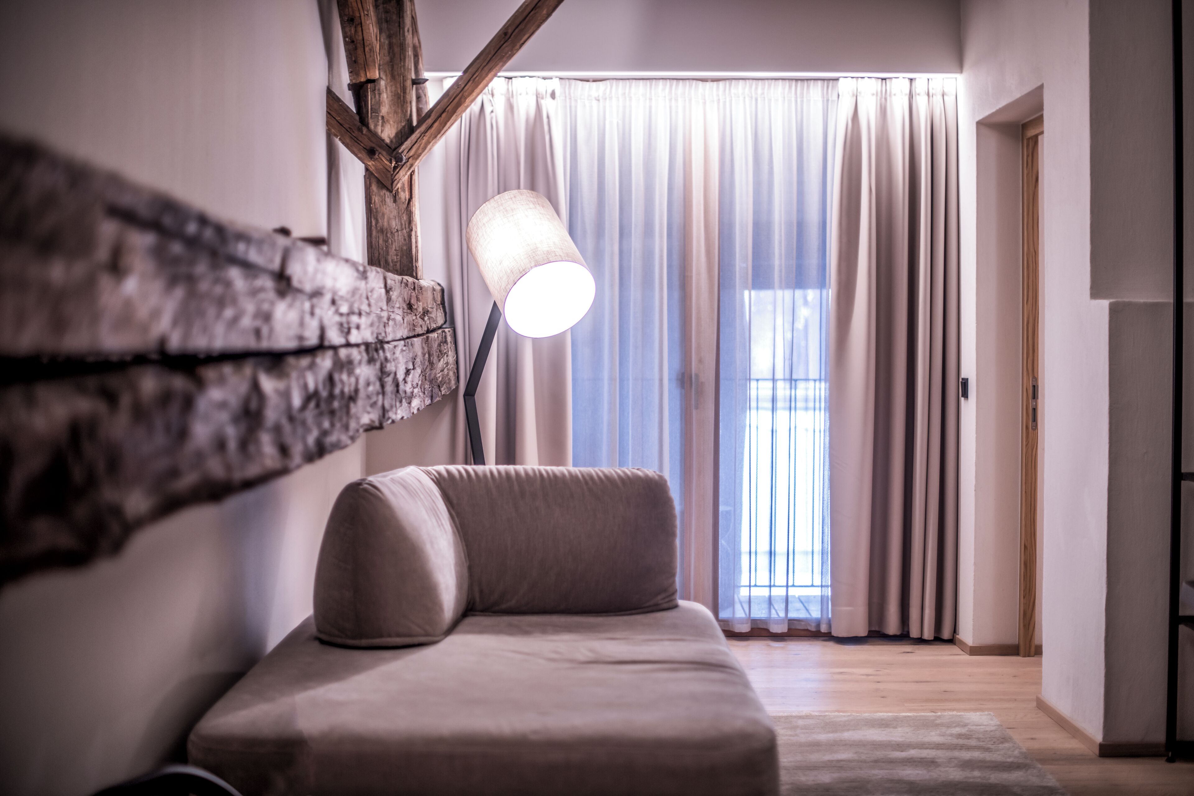 A modern room with a sofa, a lamp, and a large window with curtains.