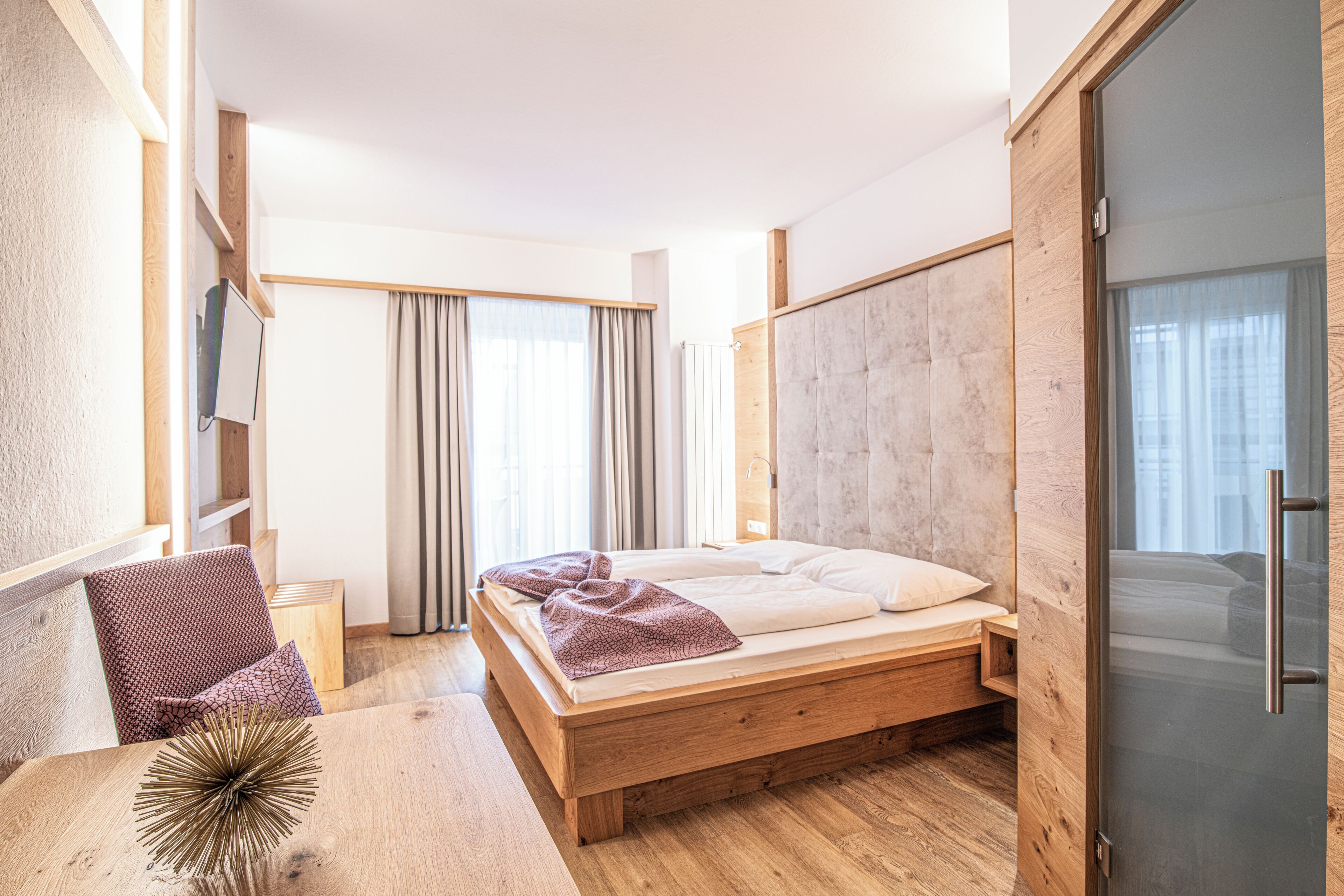 Un dormitorio moderno con una cama de madera, un escritorio, una silla y un ventanal grande.