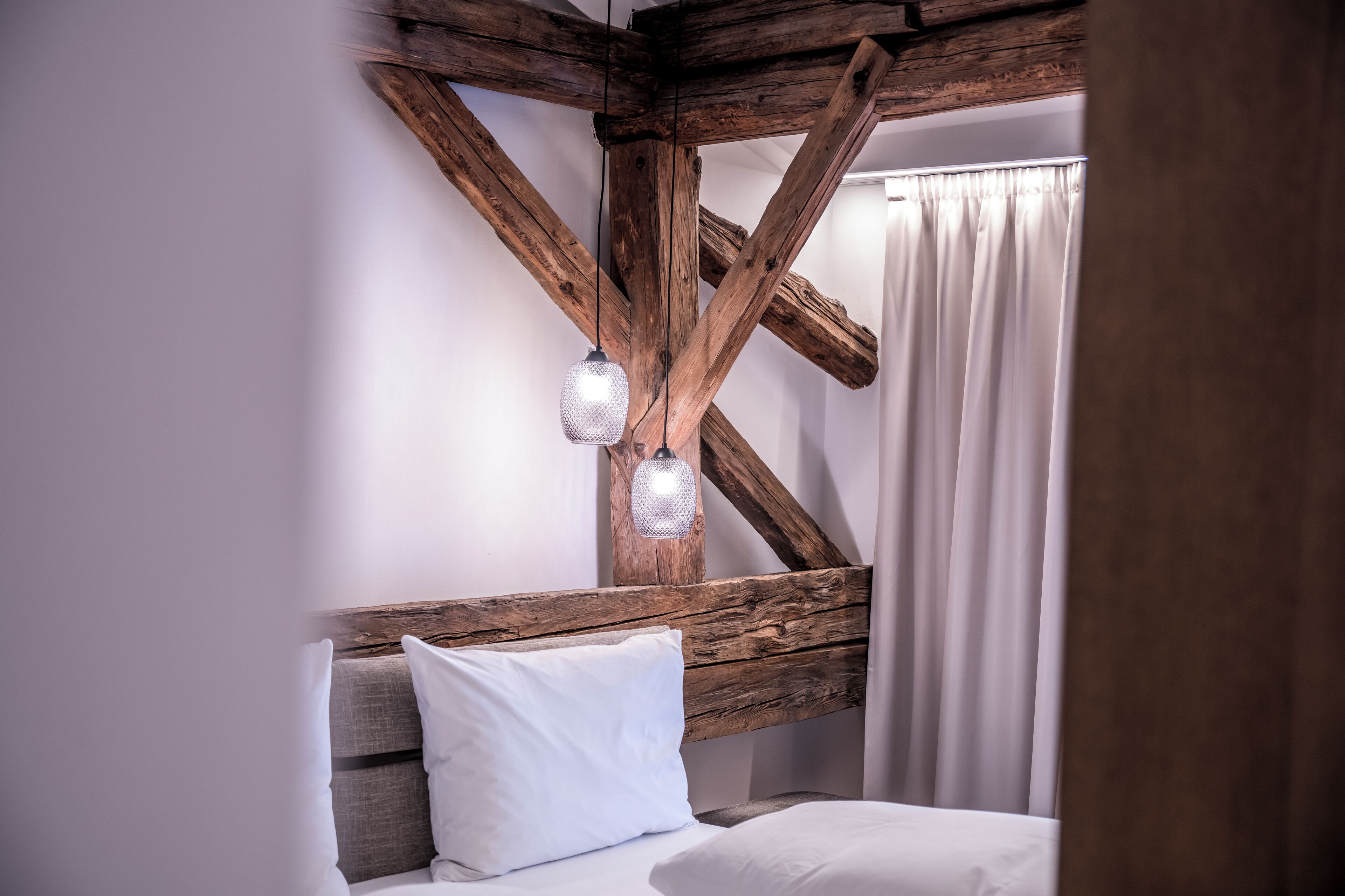 Ein Schlafzimmer mit freiliegenden Holzbalken, einem Bett mit weißer Bettwäsche und einer hängenden Lampe.