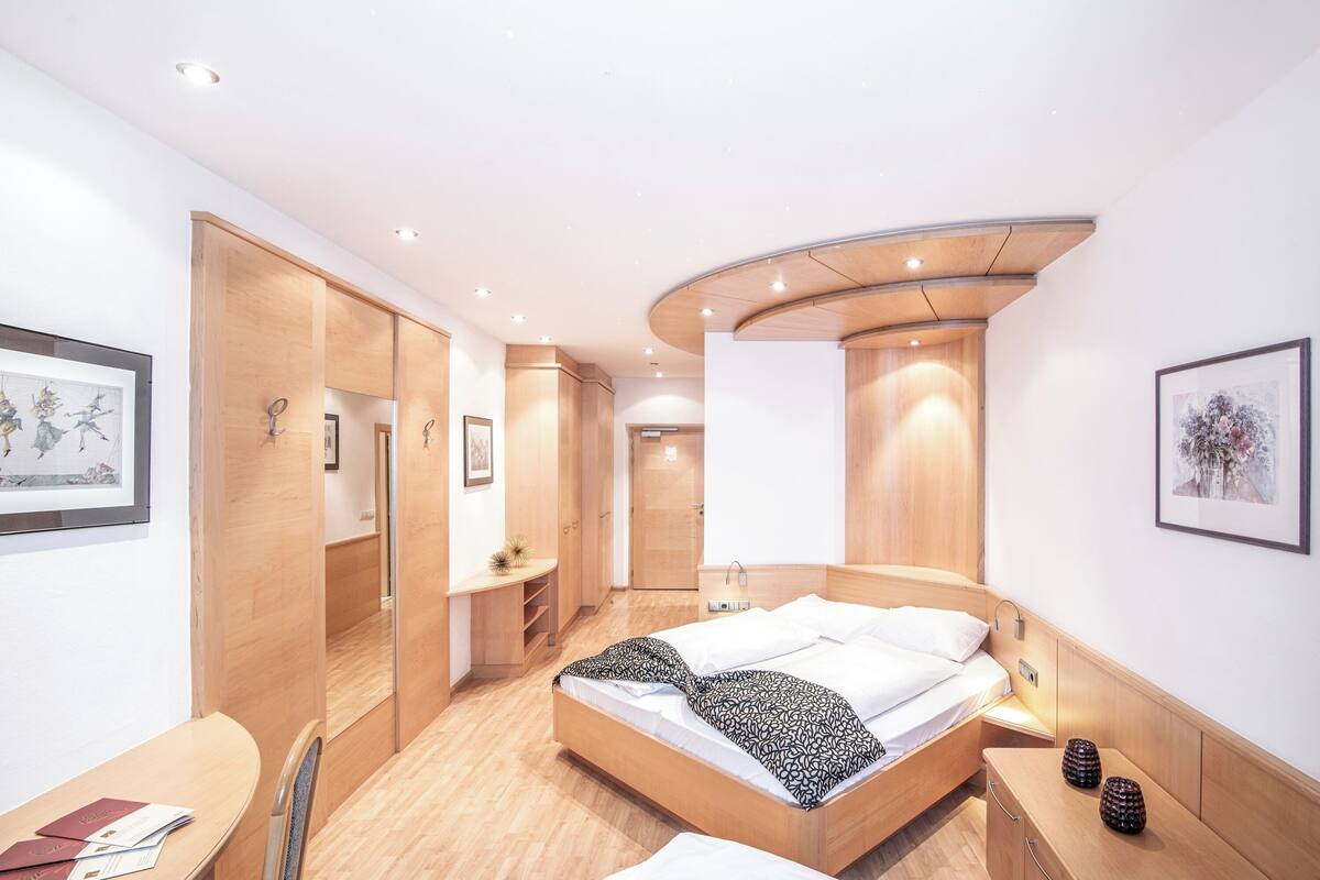 Una habitación de hotel moderna con techo curvo, una cama con manta estampada, un escritorio con silla y una mesita con objetos decorativos.