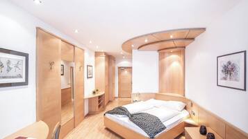 Ein modernes Hotelzimmer mit gewölbter Decke, einem Bett mit gemustertem Überwurf, einem Schreibtisch mit Stuhl und einem kleinen Tisch mit Dekoration.