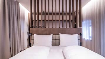 A hotel room with a large bed, curtains, a wooden headboard, and a wall-mounted shelf.