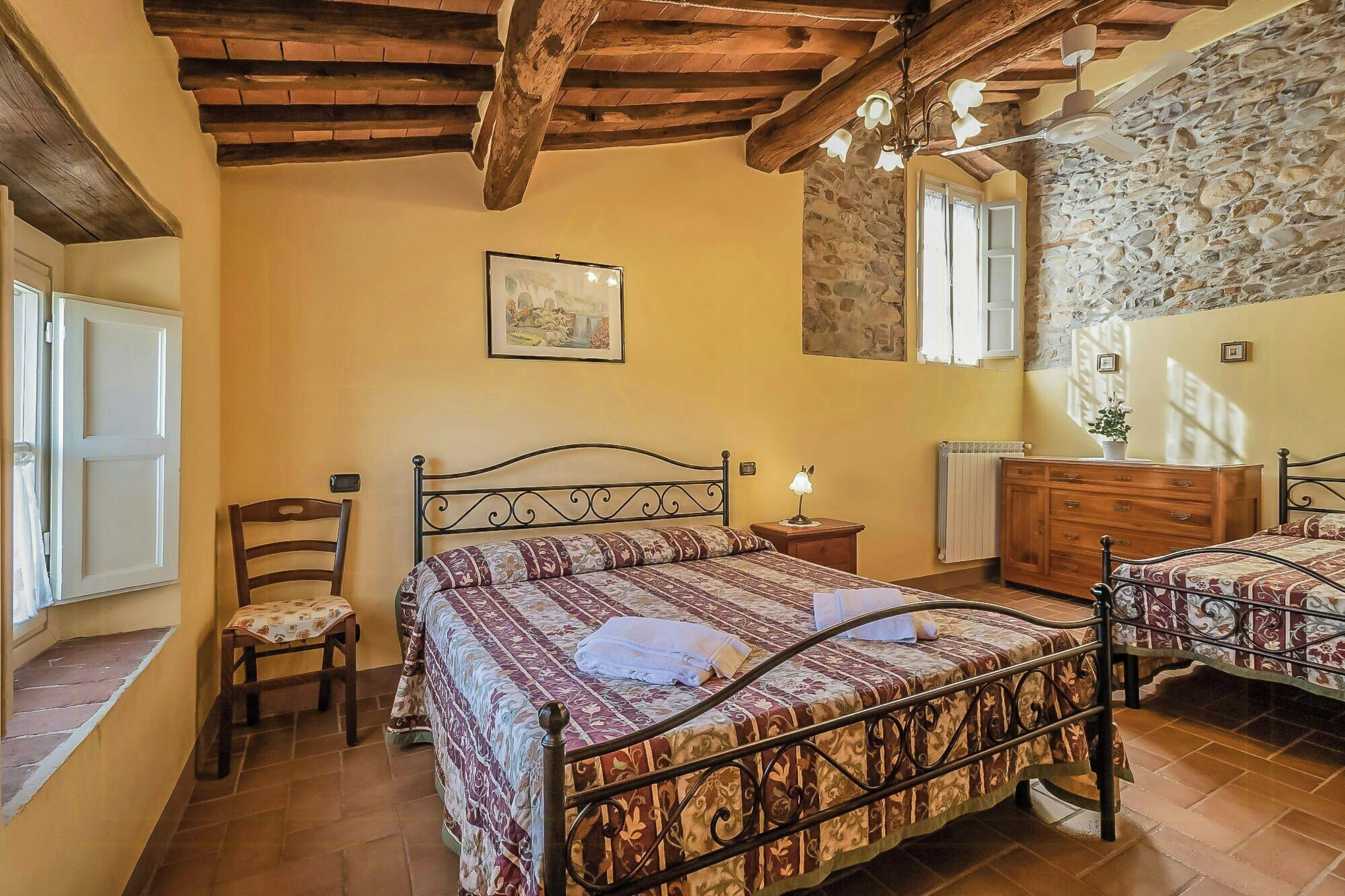 A bedroom with a bed, a chair, a dresser, a mirror, and a stone wall.