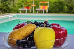 Un panier de fruits contenant une banane, des raisins et des pommes, posé sur une table près d’une piscine.