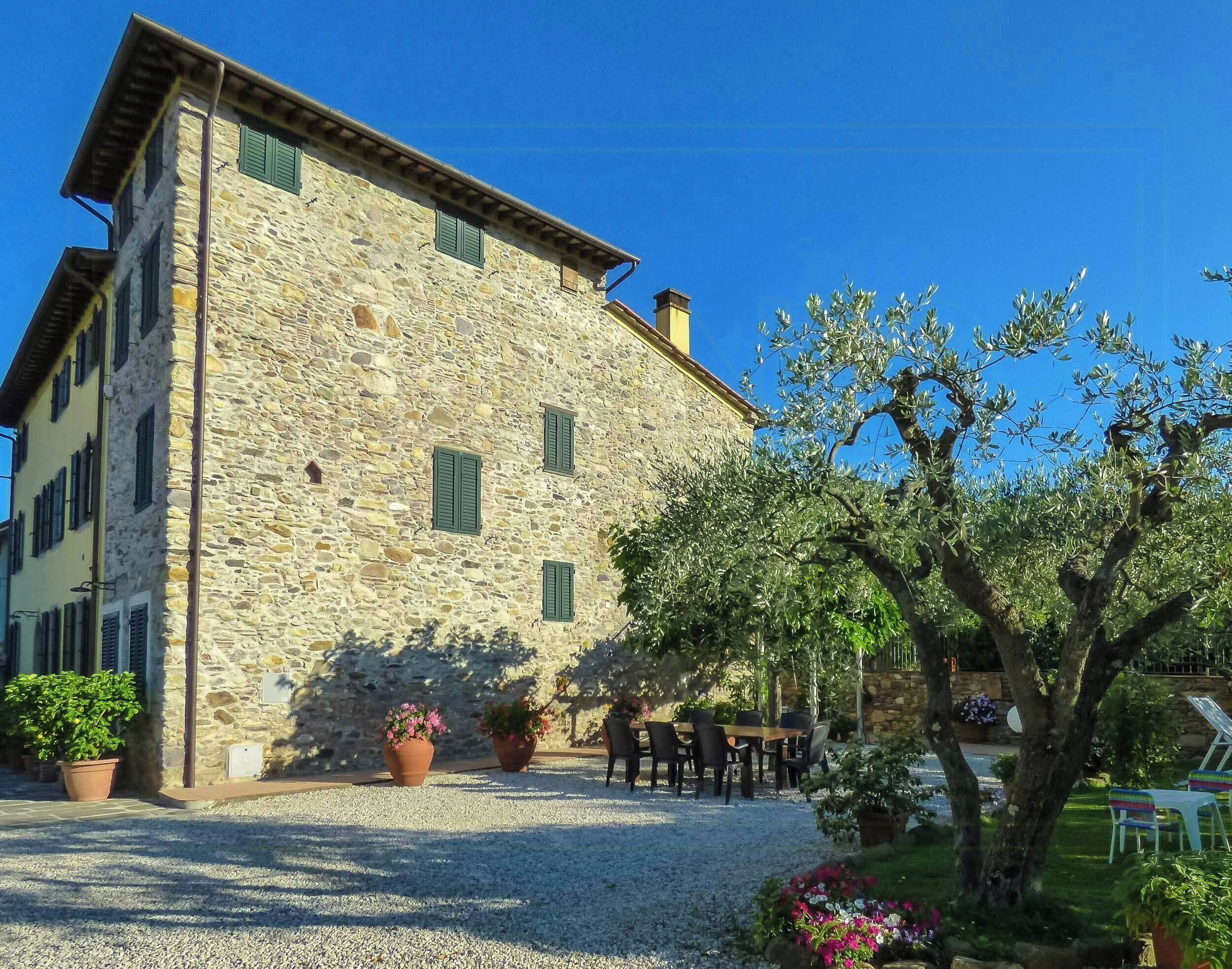 A stone building with a gravel driveway, outdoor seating, and a tree.