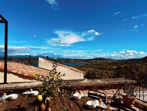 A dining table set outdoors with a scenic view of mountains and a lake. - Stone house by Lake Salagou (Liausson)