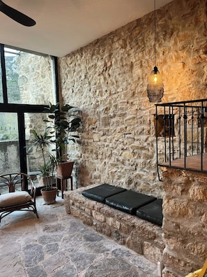 A stone-walled room with a bench, potted plants, and a hanging light fixture. - Stone house by Lake Salagou (Liausson)