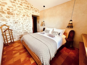 A bedroom with a stone wall, a wooden bed, a hanging chair, and a wooden floor. - Stone house by Lake Salagou (Liausson)