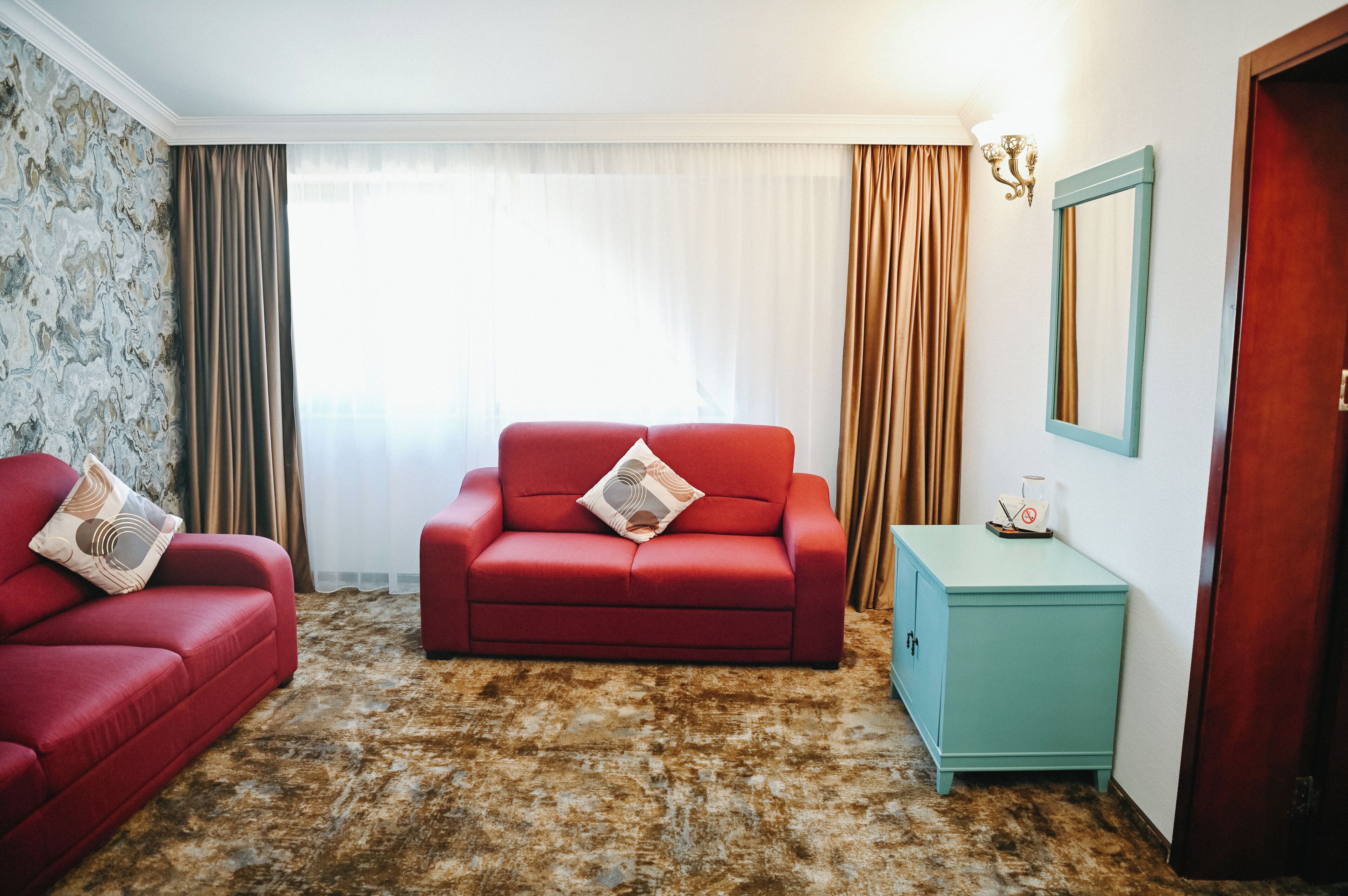 Una habitación con un sofá rojo, un aparador verde azulado y una alfombra estampada.
