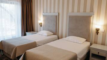 A hotel room with two beds, a nightstand, and a window with curtains.