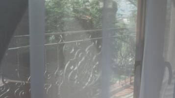 A balcony with a metal railing, a white chair, and a view of trees and a building in the background.