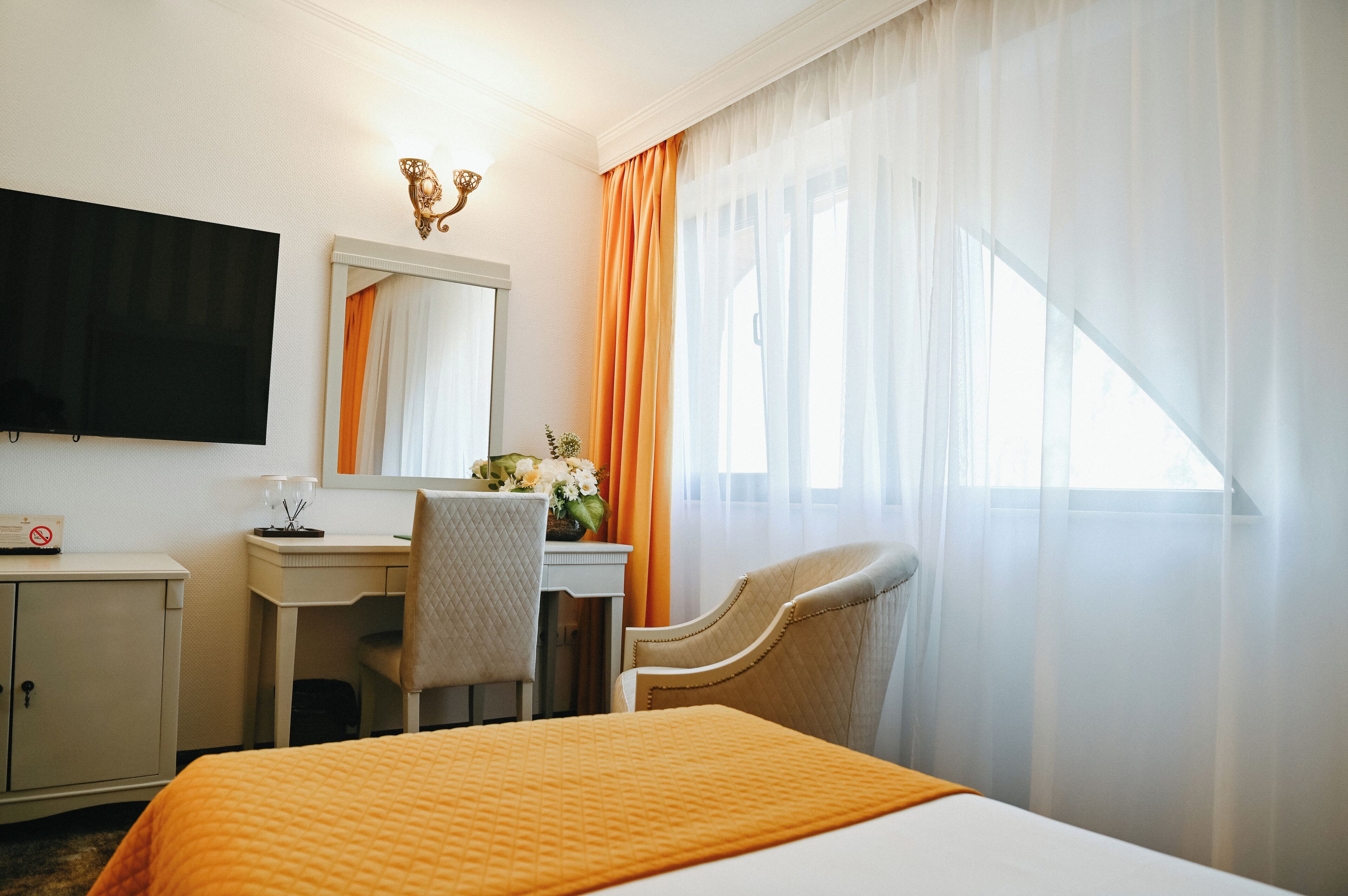 A hotel room with a bed, a desk, a chair, a television, and a window with curtains.