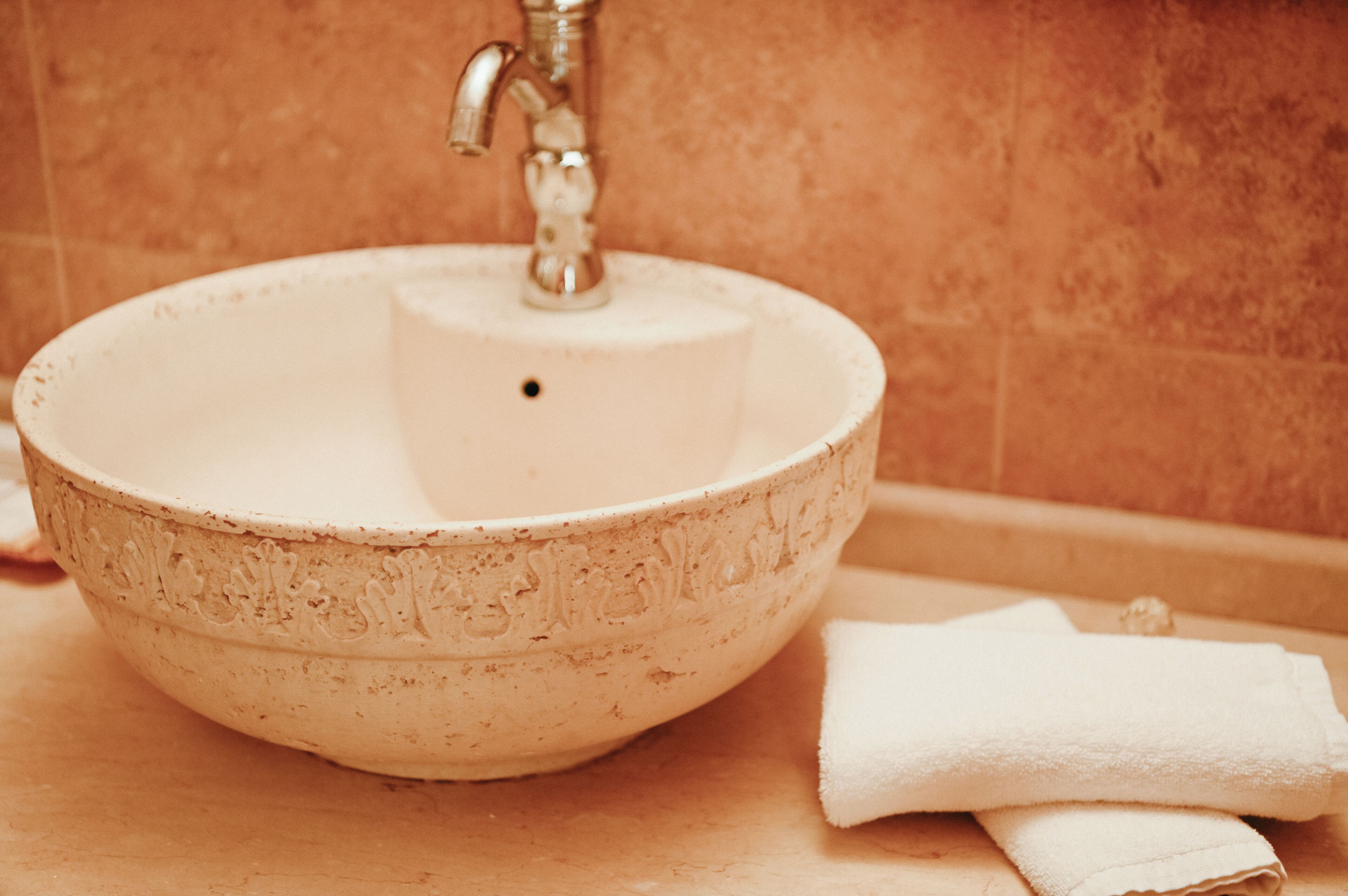 A round ceramic sink with a faucet, a white towel, and a tiled wall.
