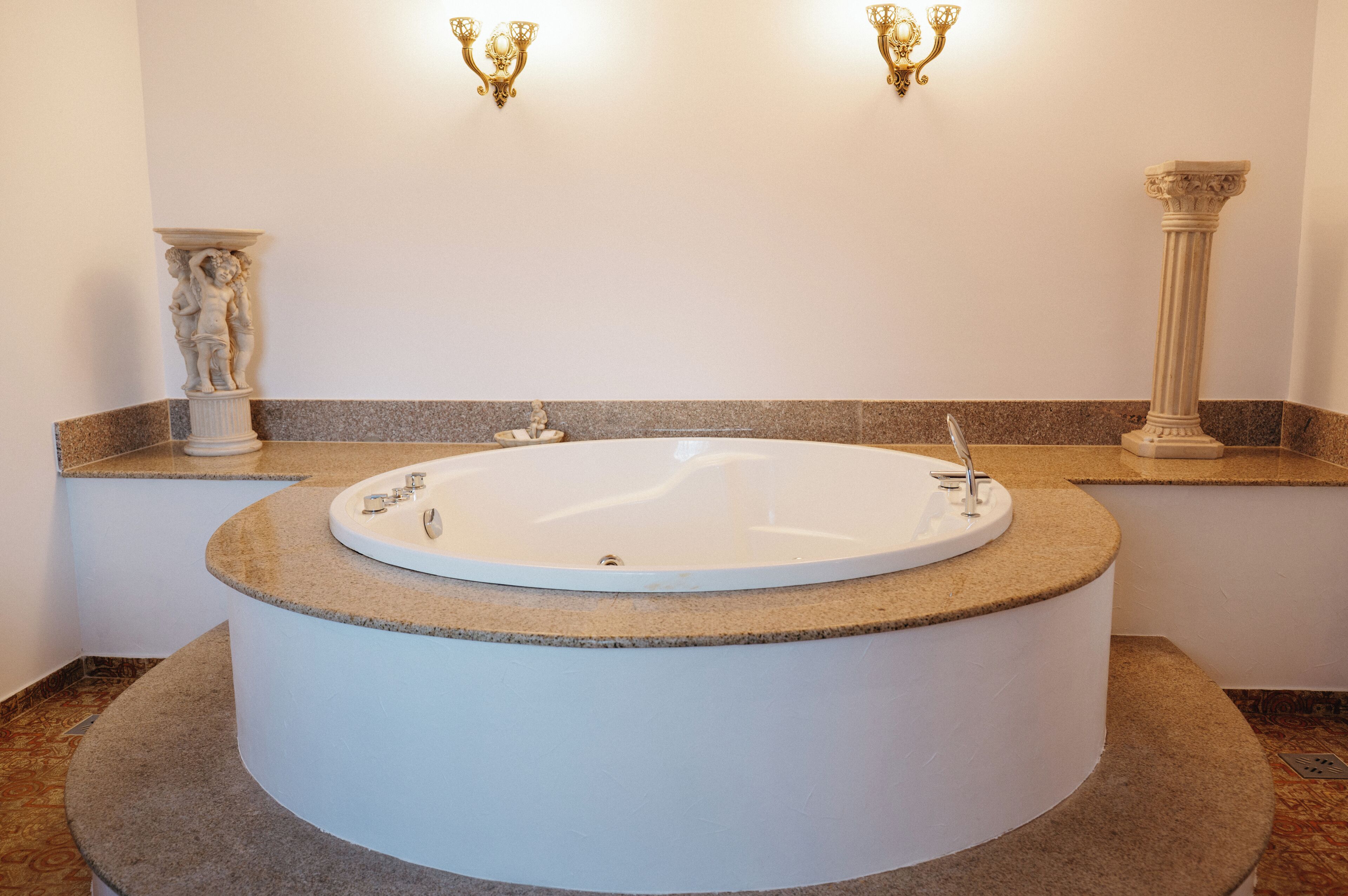 A bathroom with a freestanding bathtub, marble countertops, wall-mounted sconces, and classical-style columns.